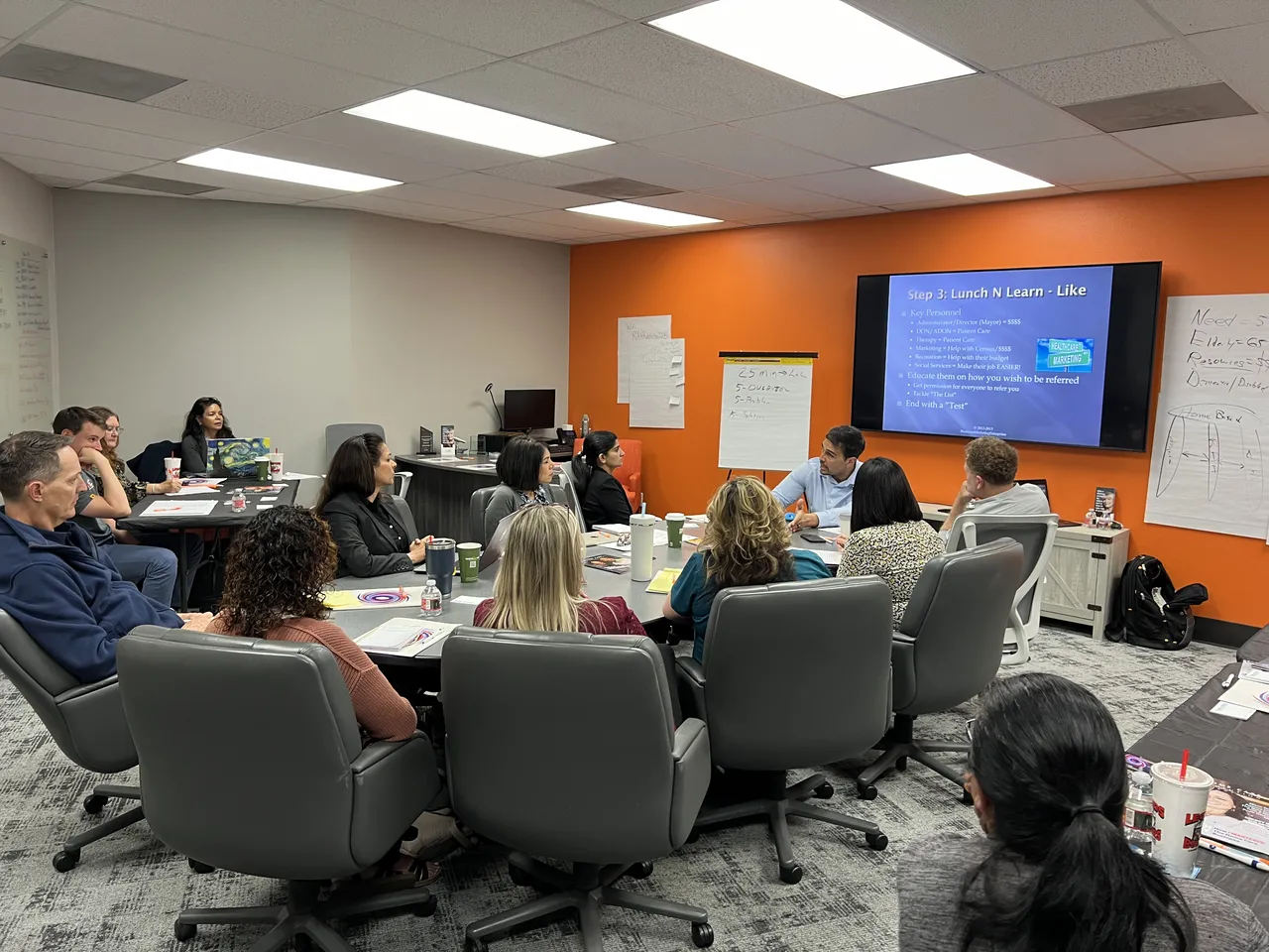 Training session with several employees gathered in a meeting room with orange walls and a screen.