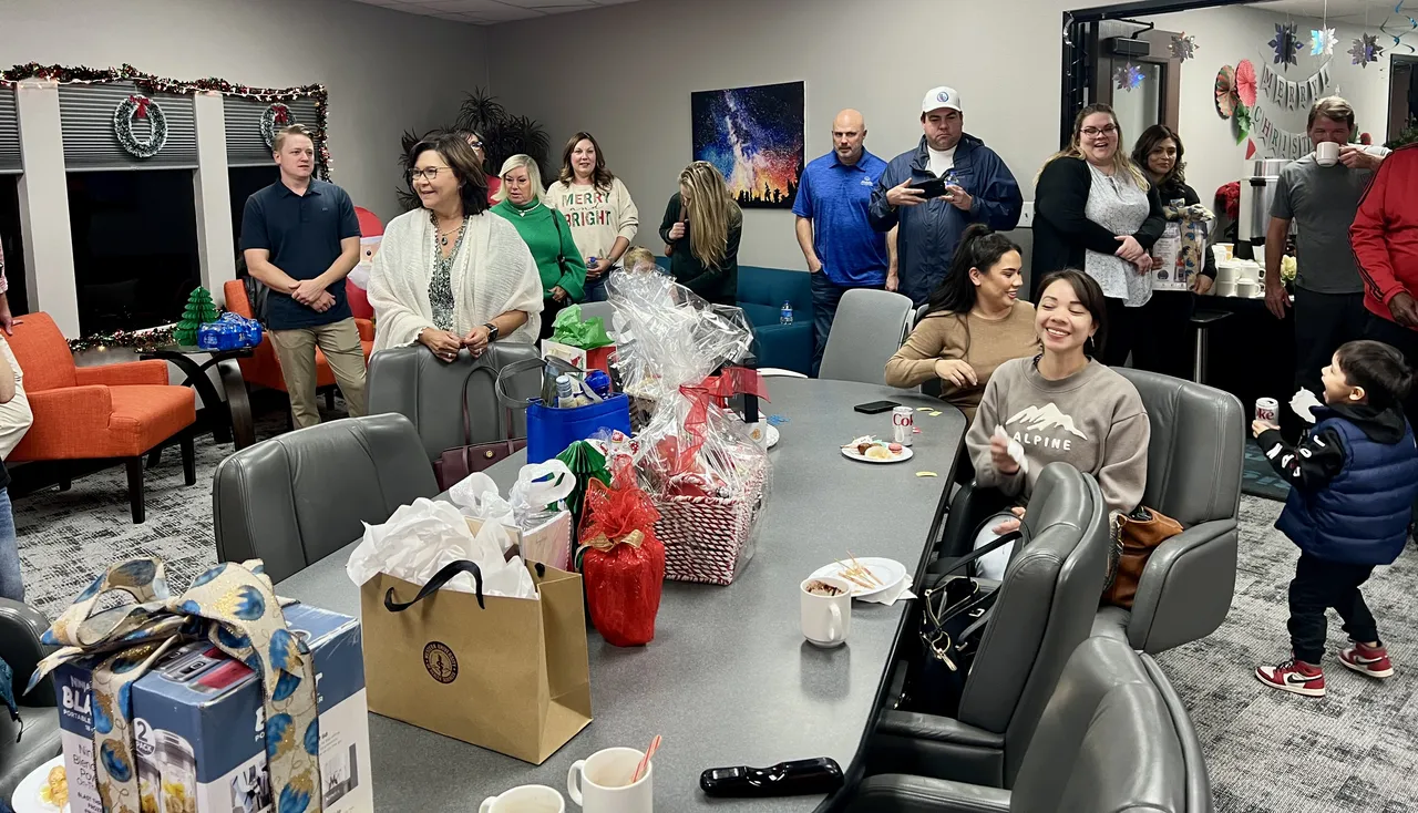 Many employees and guests gather at a holiday party inside an office.